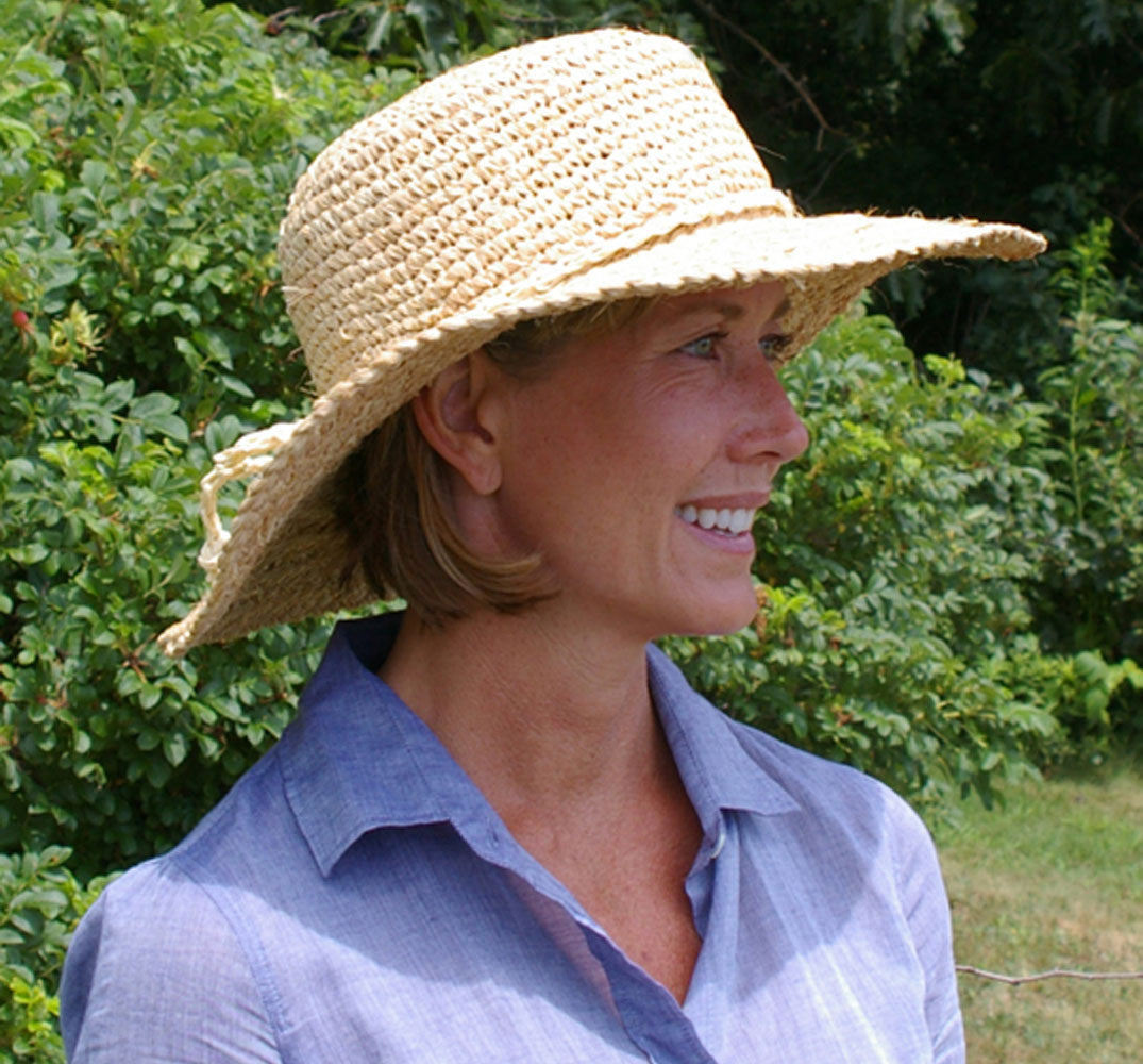 Woman wearing a straw hat and blue shirt outdoors with greenery in the background