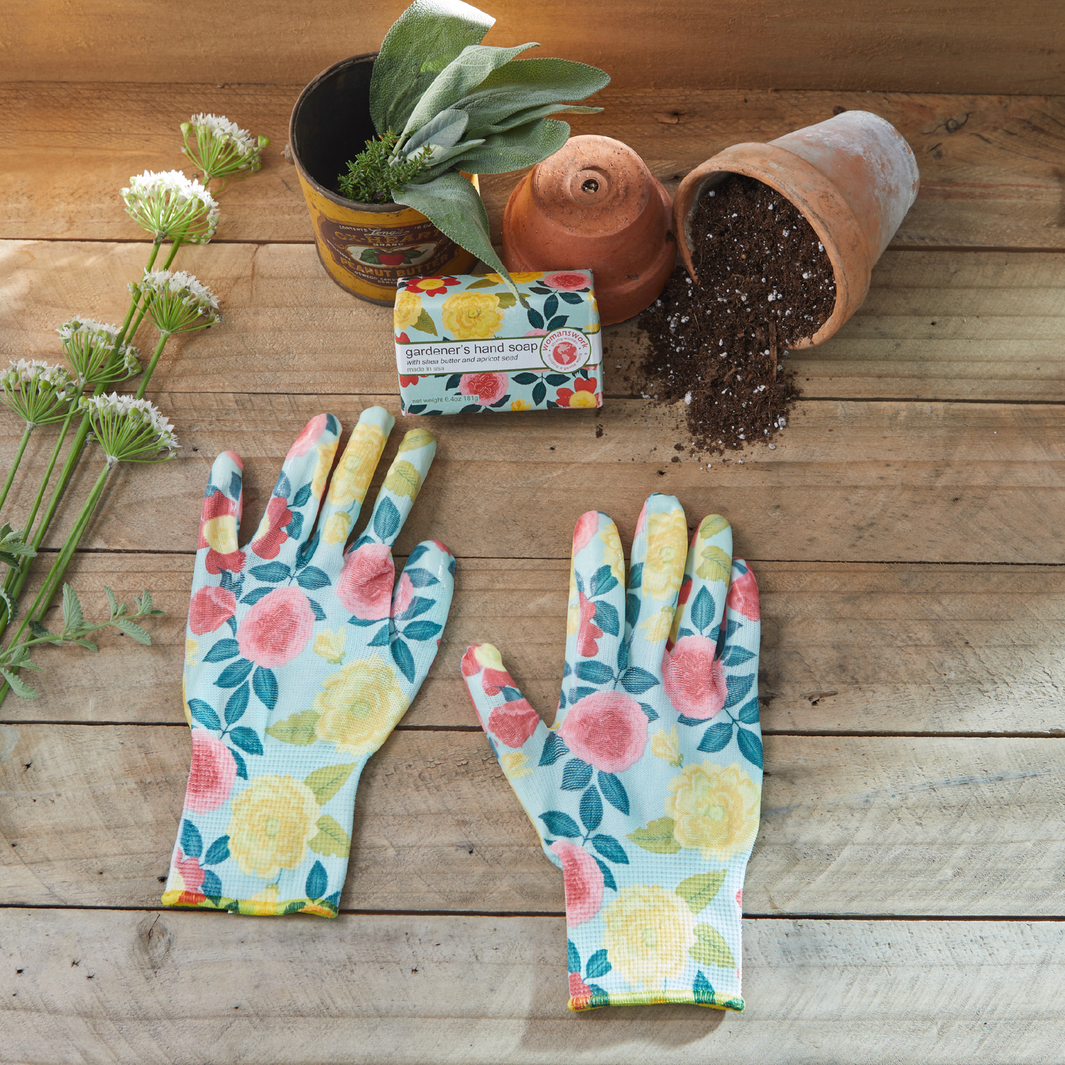 Floral gardening gloves on a wooden surface with plants and pots.