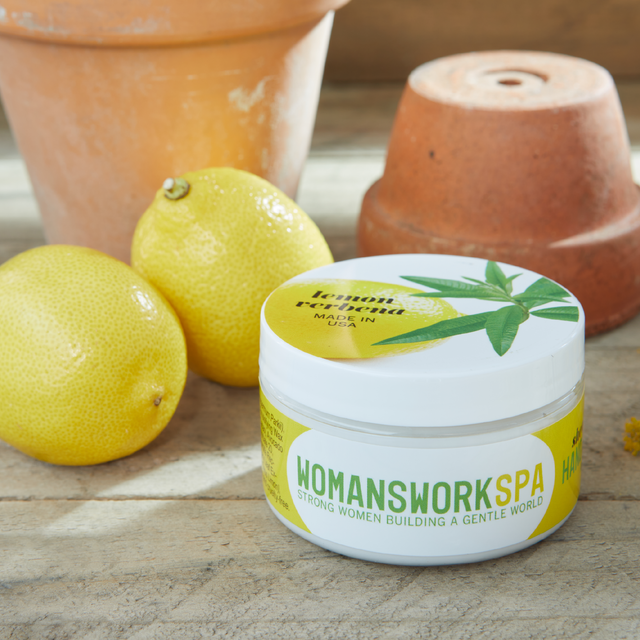 Jar of 'Womanswork Spa' product with lemons and terracotta pots on a wooden surface