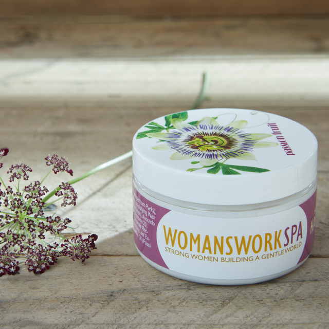 Jar of 'Womanswork Spa' product on a wooden surface with flowers.