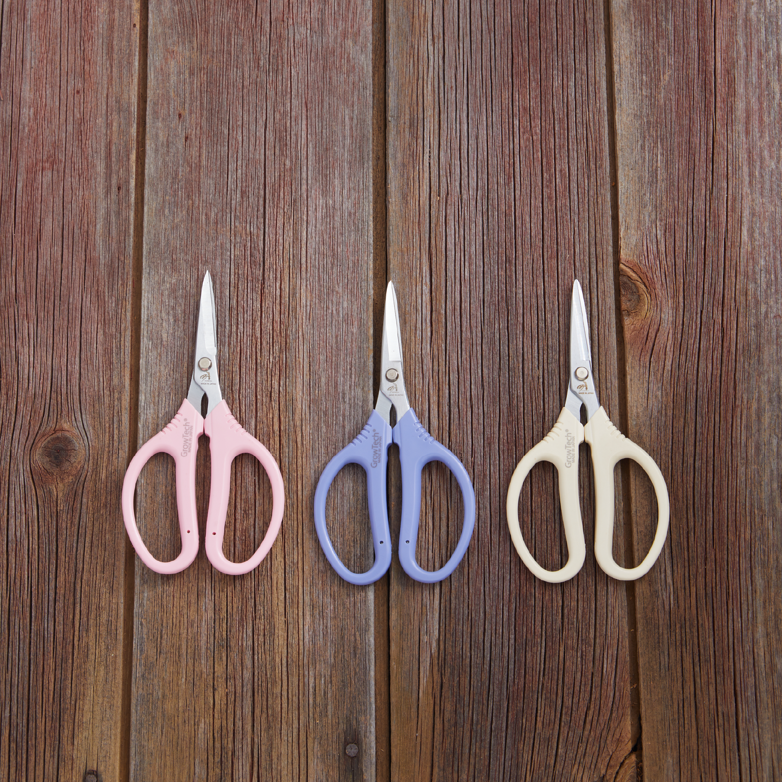 Three pairs of scissors with different colored handles on a wooden surface