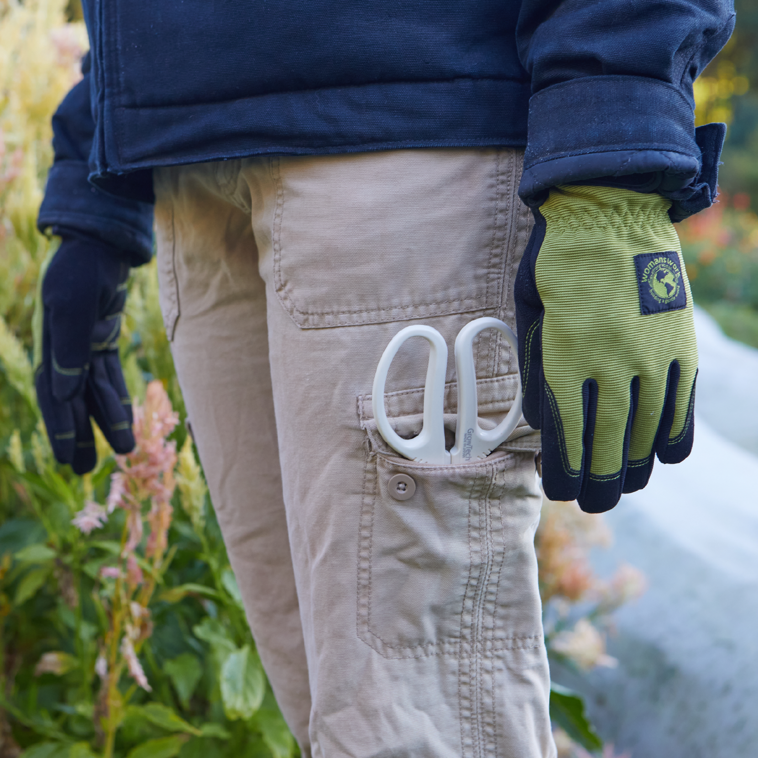 Person wearing gardening gloves with a garden tool in pocket, standing in a garden.