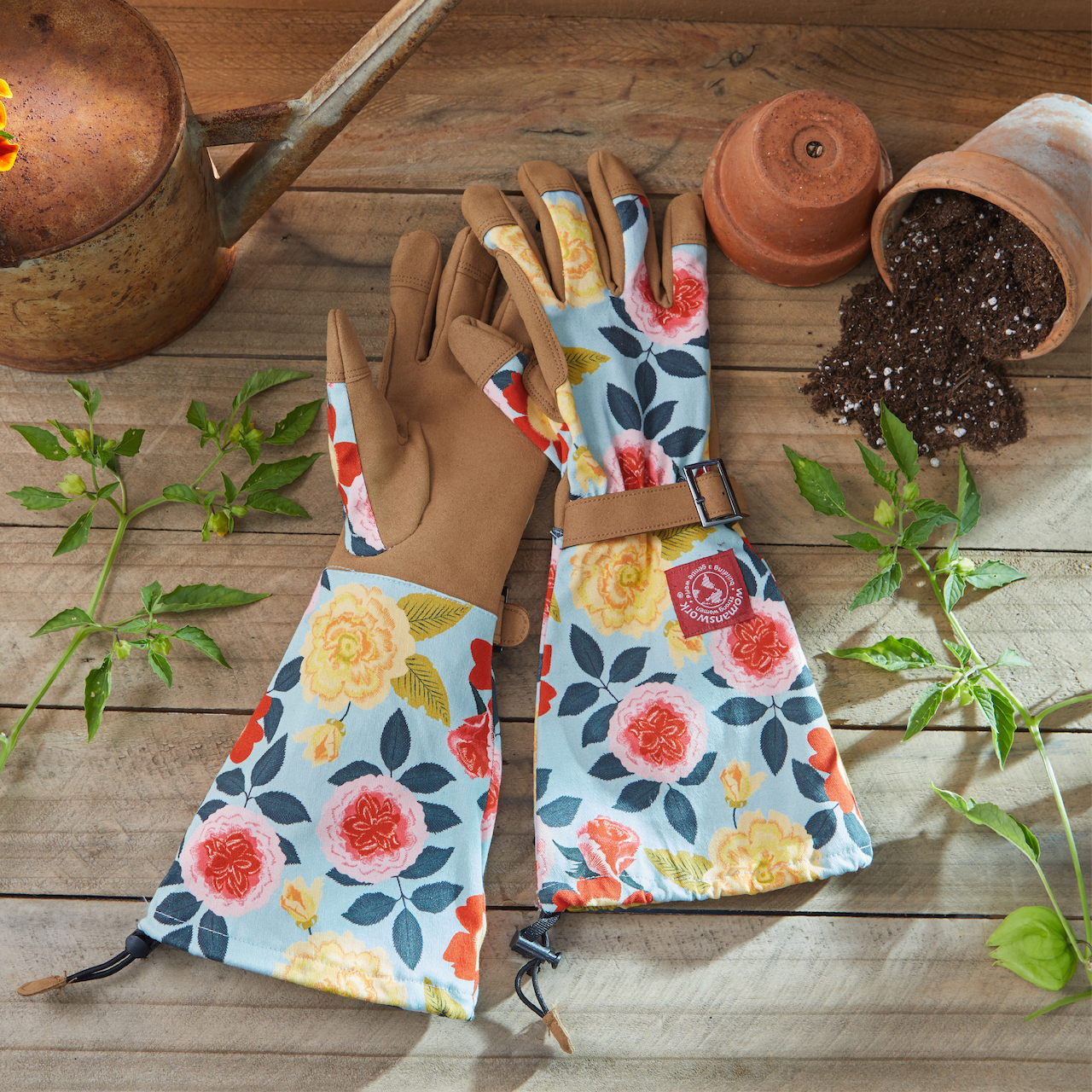 Gardening gloves with floral patterns on a wooden surface with gardening tools and plants.