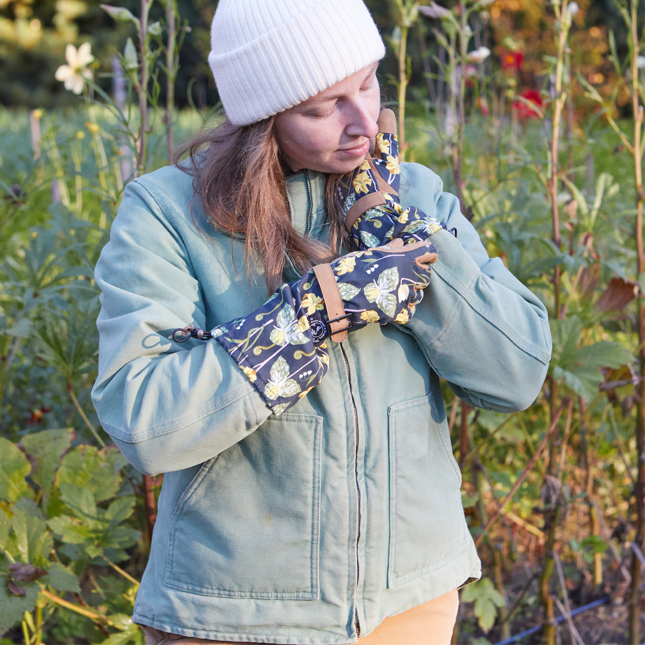 Person wearing a colorful gloves and white beanie in a field with greenery.