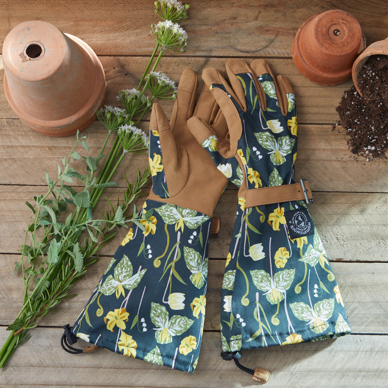 Floral-patterned gardening gloves on a wooden surface with plants and pots.