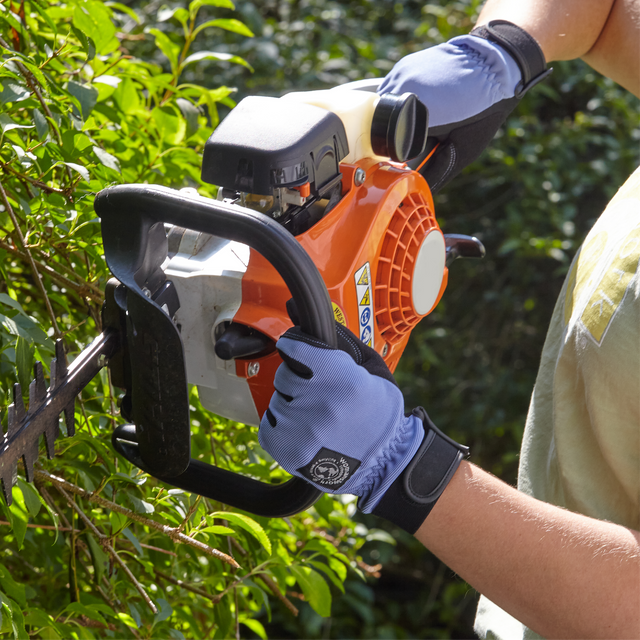 Person using a chainsaw to trim bushes with gloves on