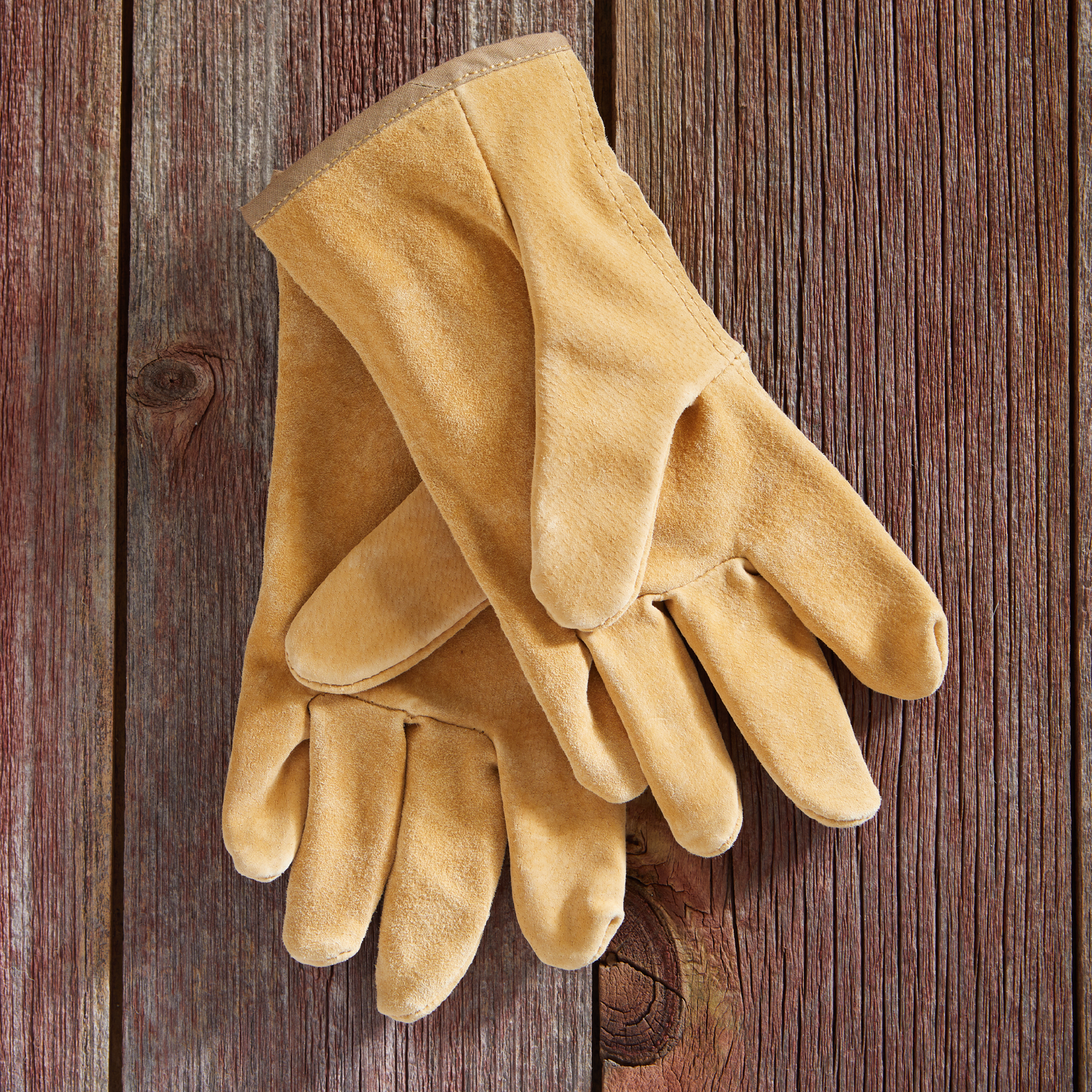 Pair of tan work gloves on a wooden surface