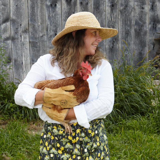 Woman wearing a hat holding a chicken outdoors with a wooden fence in the background