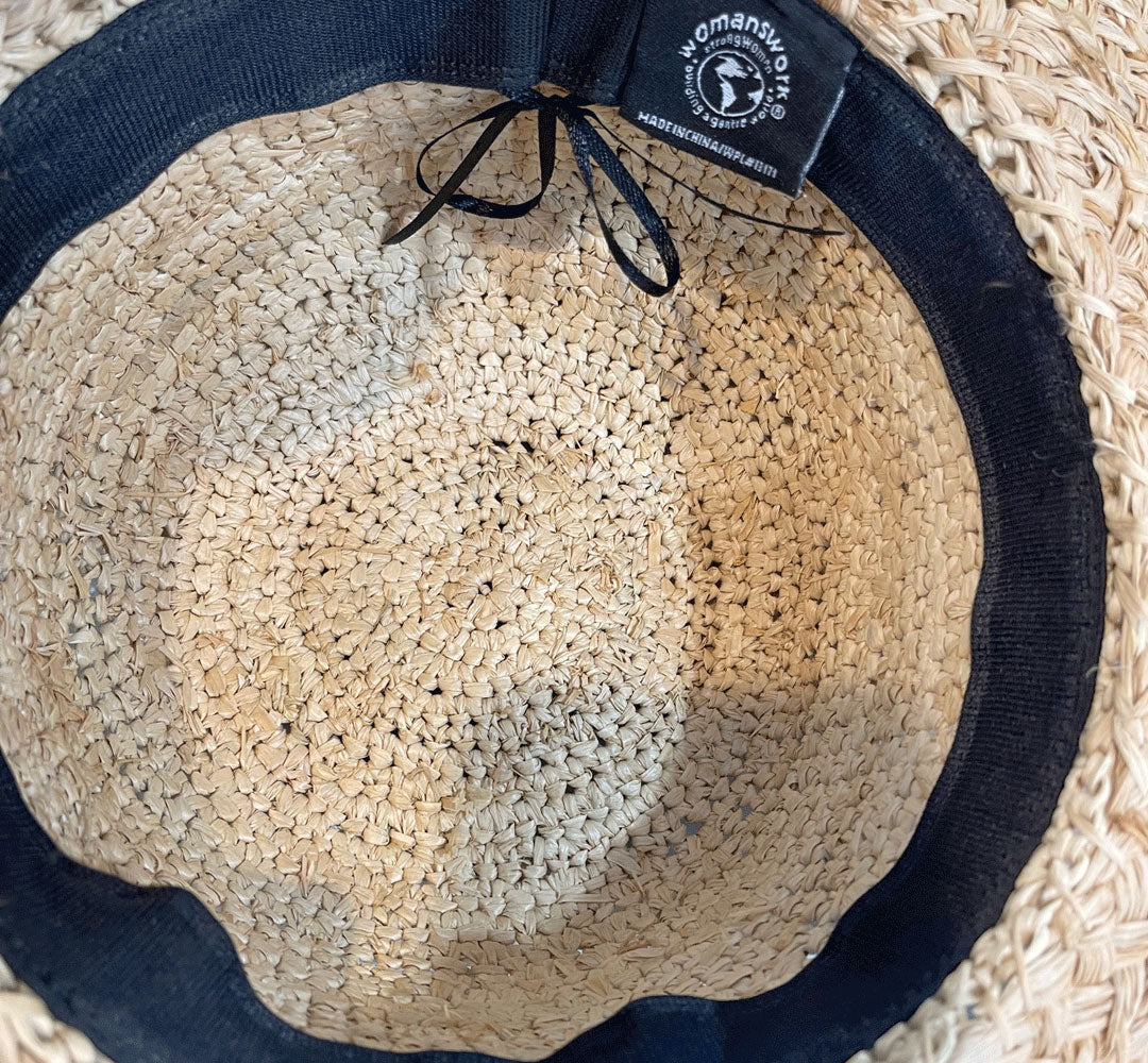 Straw hat with navy band and 'Womanshu' brand tag on a woven surface
