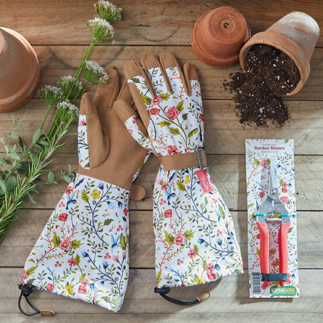 Gardening gloves with floral pattern, garden shears packaging, and soil on a wooden surface