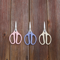 Three pairs of scissors with different colored handles on a wooden surface