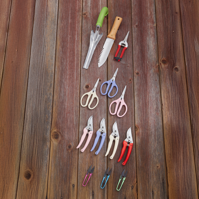 Set of gardening tools including pruners, shears, and a knife on a wooden surface.