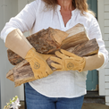 Person holding a bundle of firewood wearing tan work gloves outdoors.