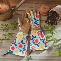 Gardening gloves with floral patterns on a wooden surface with gardening tools and plants.