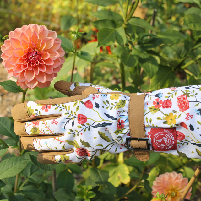 Floral gardening glove with a Womans Work label held by a pink flower in a garden setting