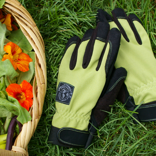 Green gardening gloves with black accents on grass next to a basket of flowers