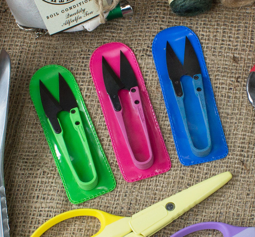 Three pairs of colorful garden shears in their respective cases on a textured surface.