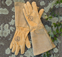 Pair of tan gardening gloves with 'Woman's Work' logo on a textured surface with greenery.